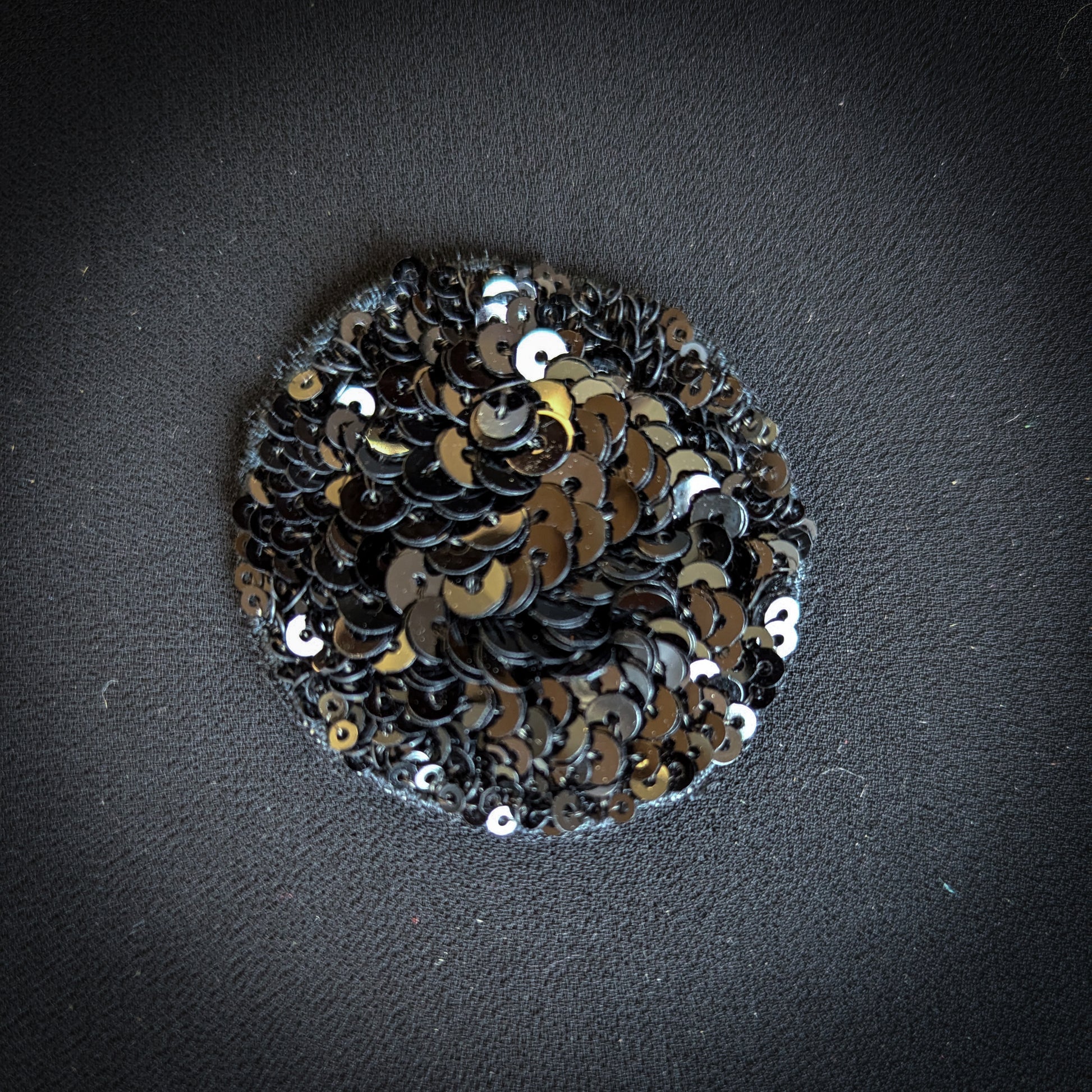 Round D&G black sequin patch, 5x5 cm, on dark fabric.