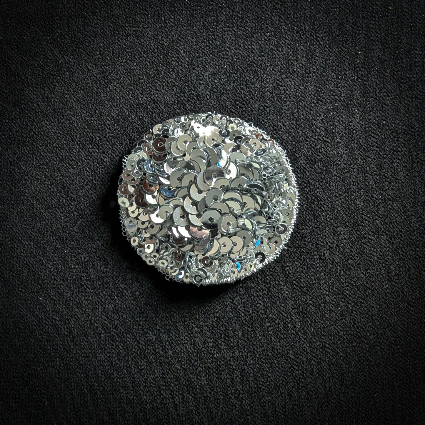Round silver sequin patch, 5x5 cm, on a black fabric background.