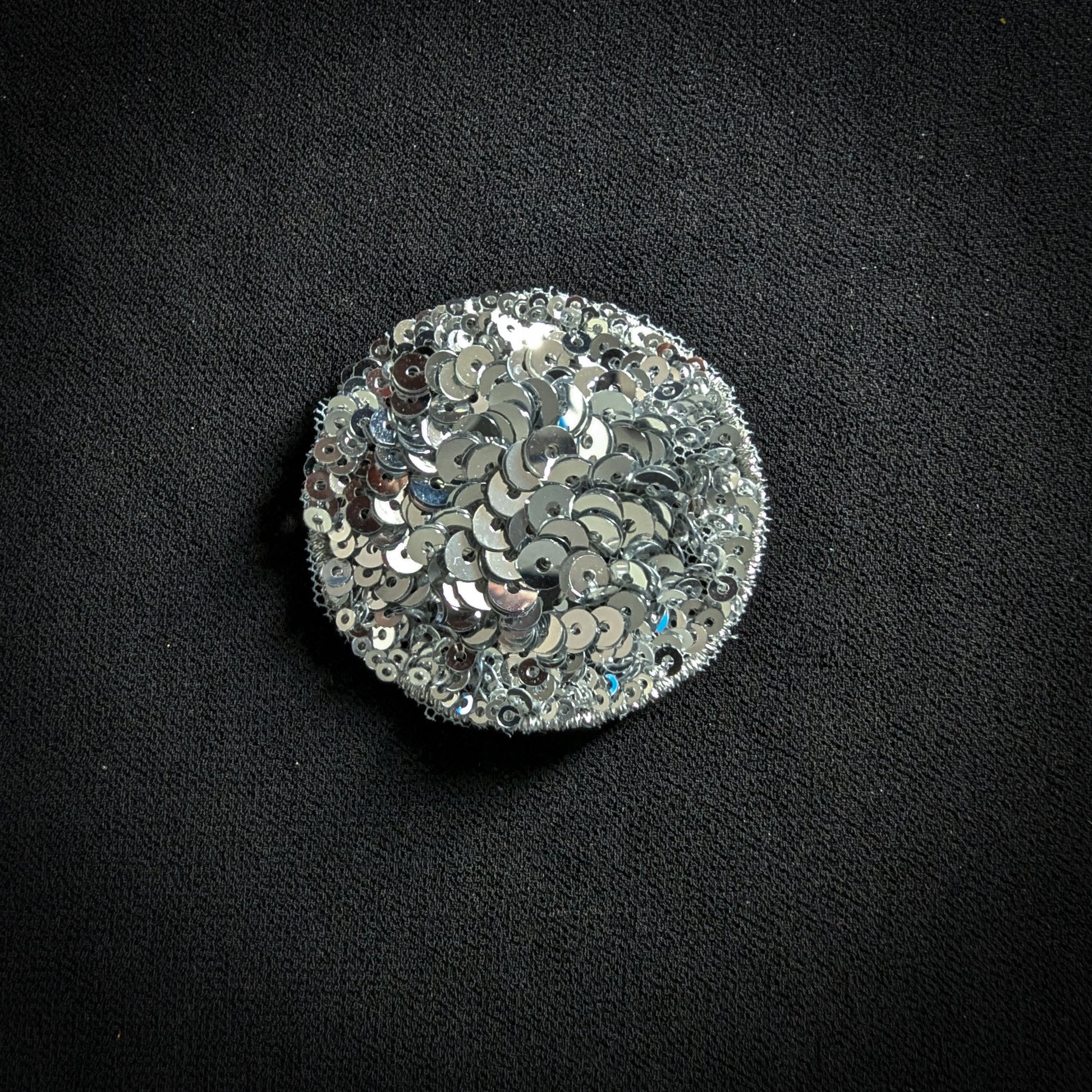 Round silver sequin patch, 5x5 cm, on a black fabric background.