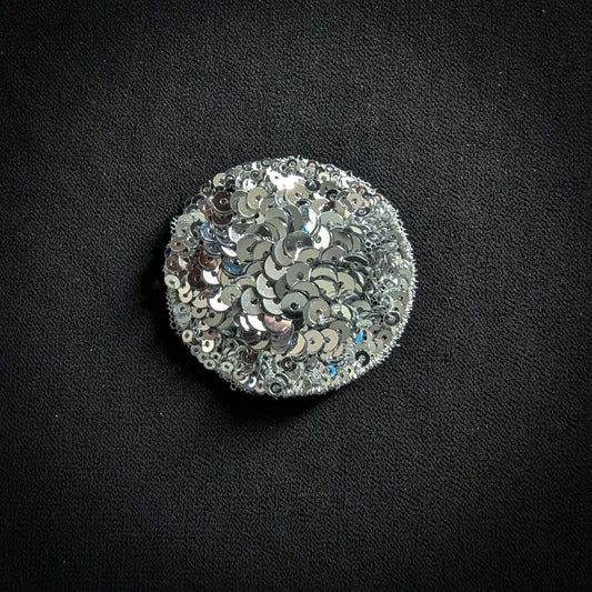 Round silver sequin patch, 5x5 cm, on a black fabric background.