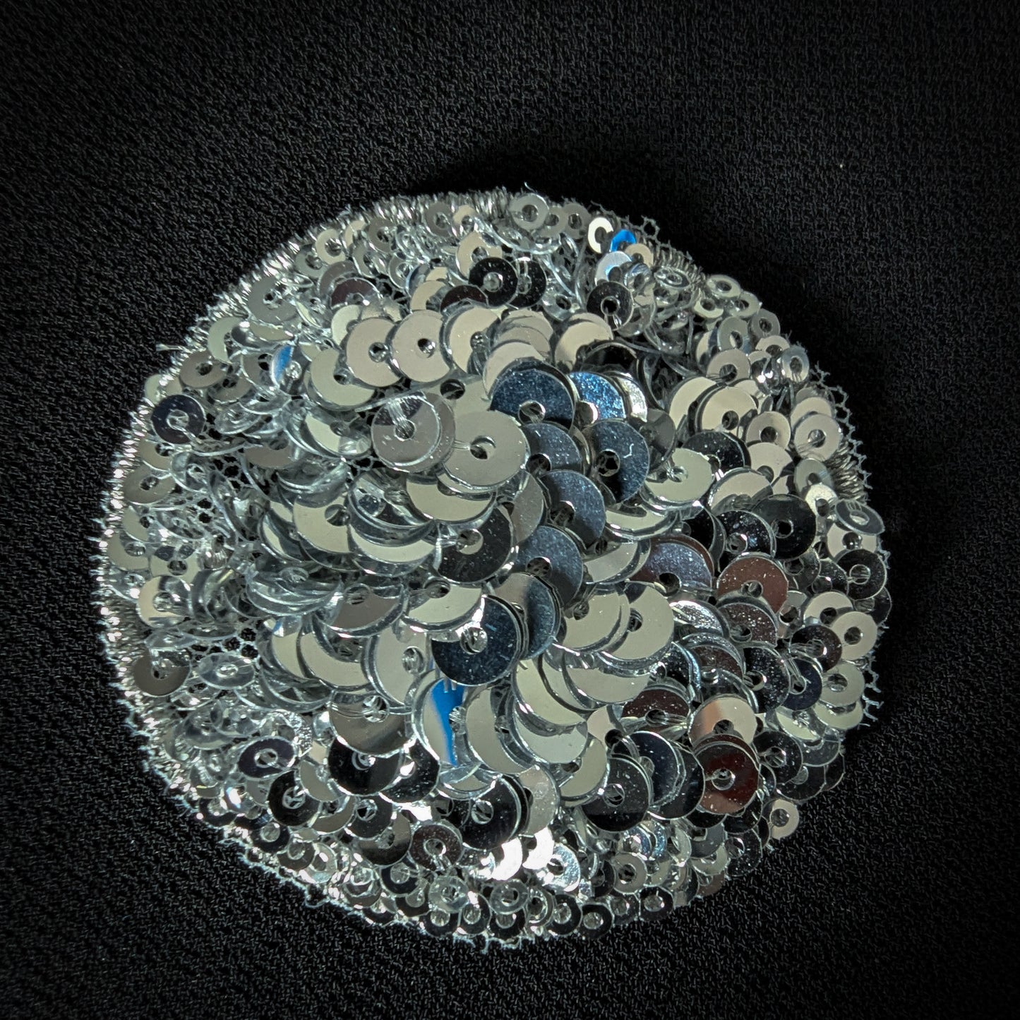 Round silver sequin patch, 5x5 cm, with a white polka dot design on black fabric.