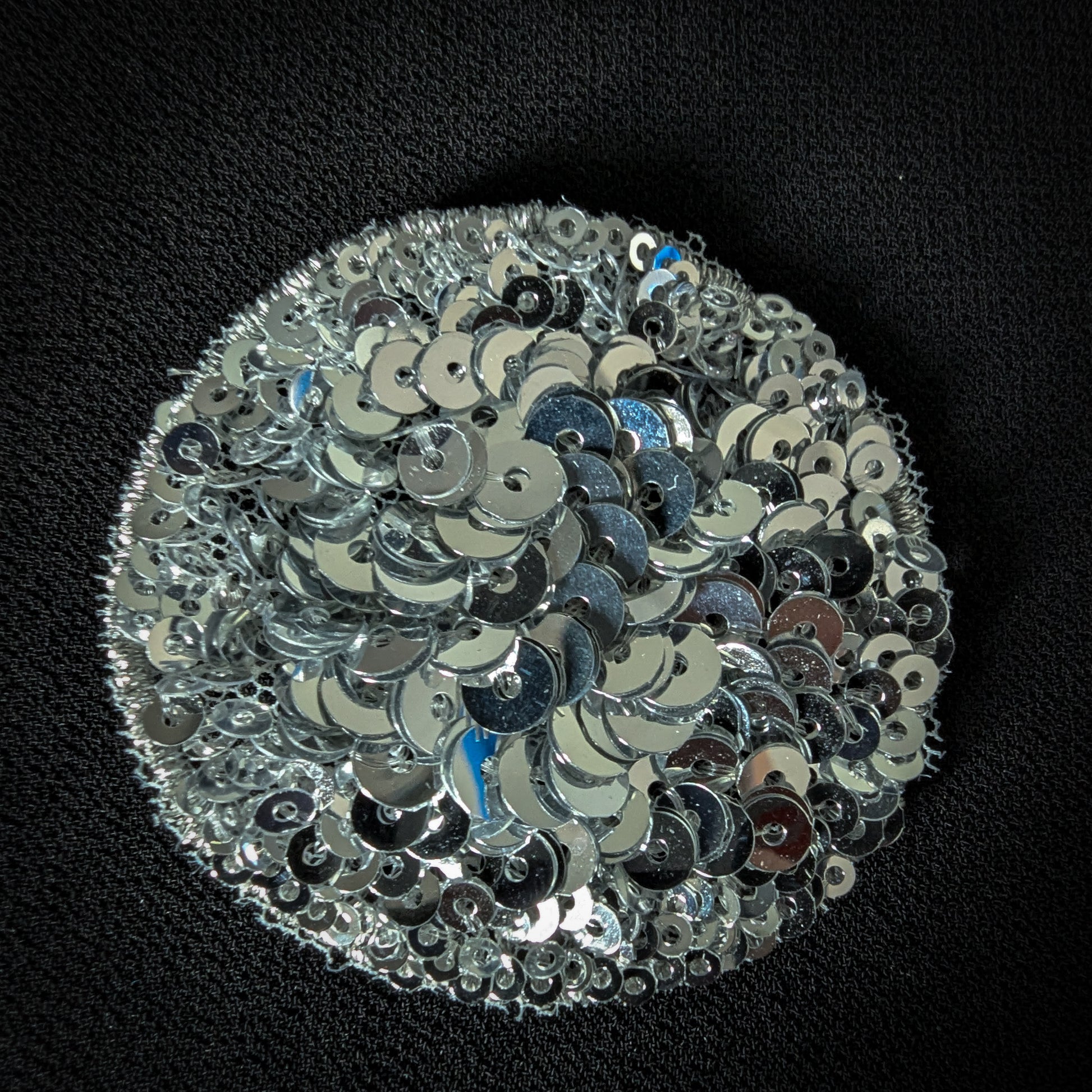 Round silver sequin patch, 5x5 cm, with a white polka dot design on black fabric.
