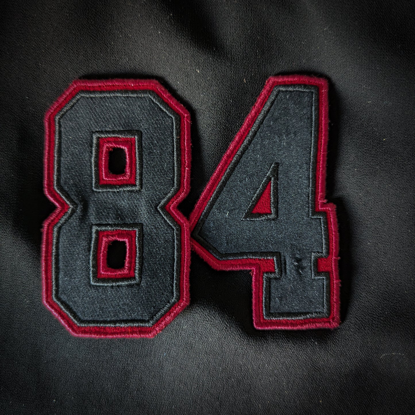 Black embroidered "84" patch with a bold red border, ideal for clothing or accessories.