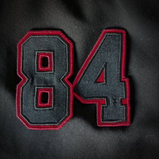 Black embroidered "84" patch with a bold red border, ideal for clothing or accessories.