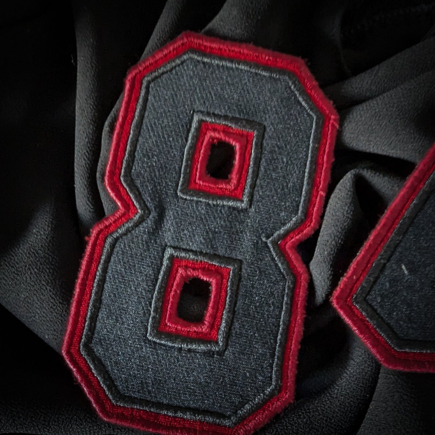 Black and red embroidered D&G "8" patch, 6x8 cm, on dark fabric.
