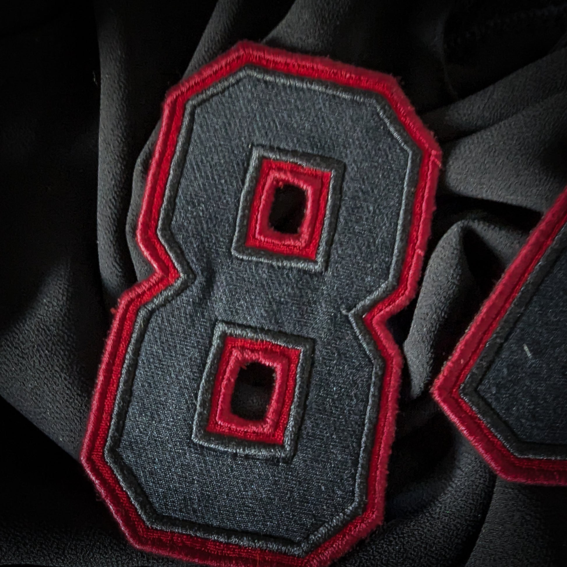 Black and red embroidered D&G "8" patch, 6x8 cm, on dark fabric.