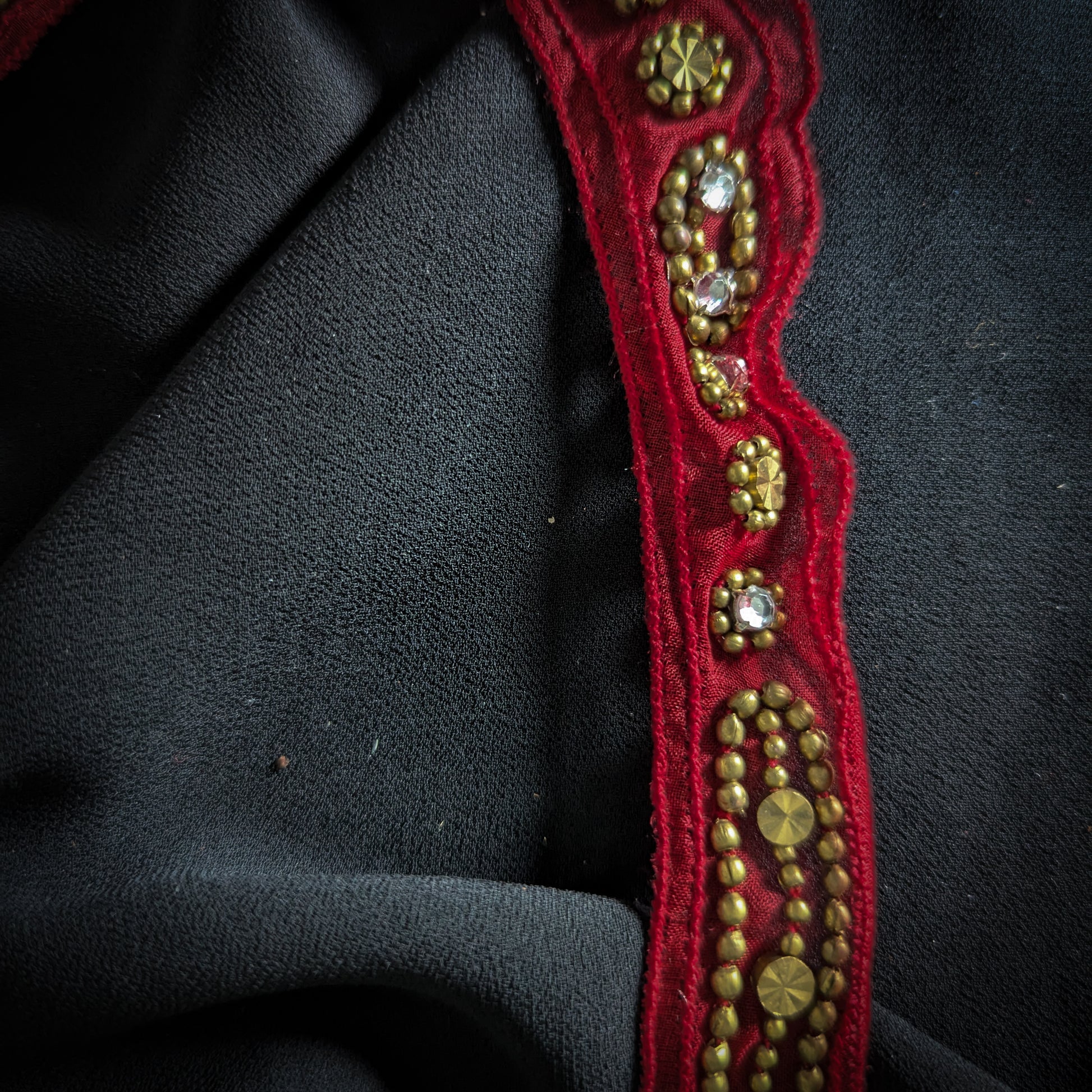 Red D&G Zierelement trim, 2cm wide, with gold beads and clear rhinestones on black fabric.