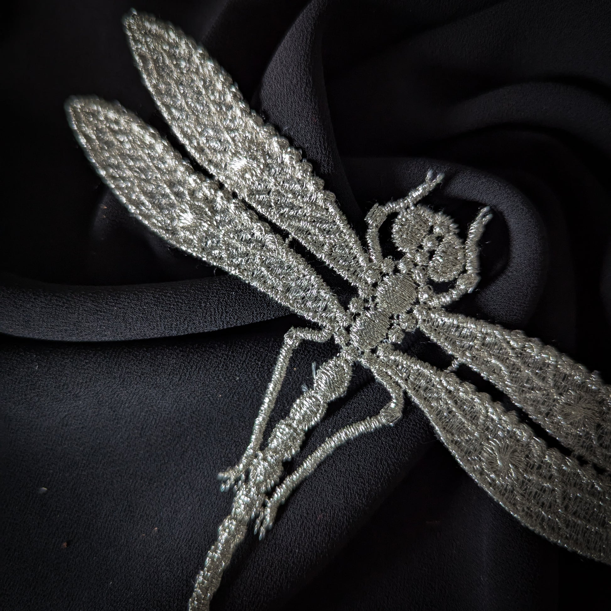 Silver embroidered dragonfly patch, 9x15cm, on a black fabric background.