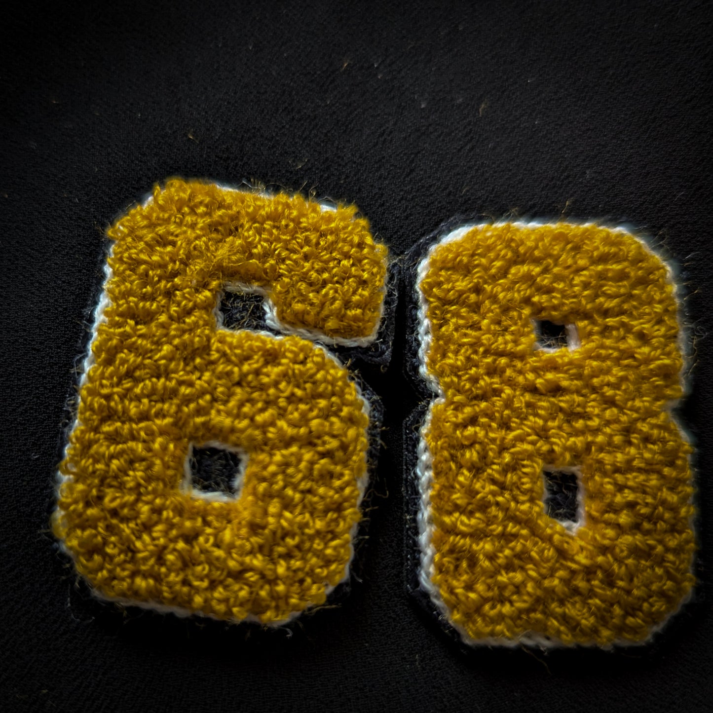 D&G gold chenille patch with "68" numbers, outlined in white and black, on a dark fabric.