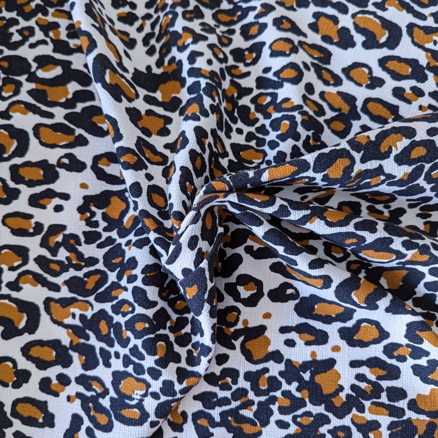 Deadstock cotton fabric with a white background and classic black and brown leopard print.