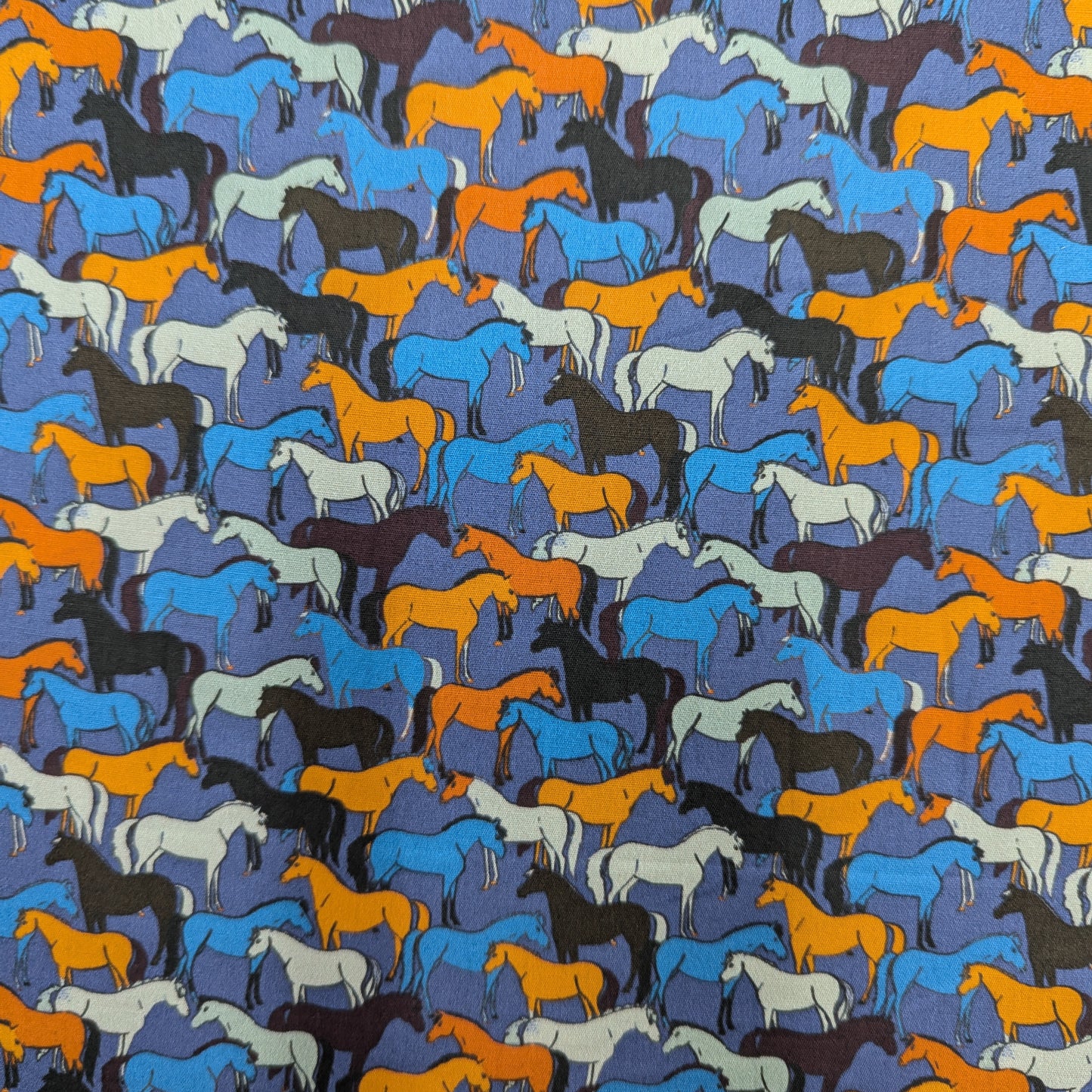 Deadstock cotton poplin fabric with a repeating pattern of colorful horse silhouettes on a blue background.
