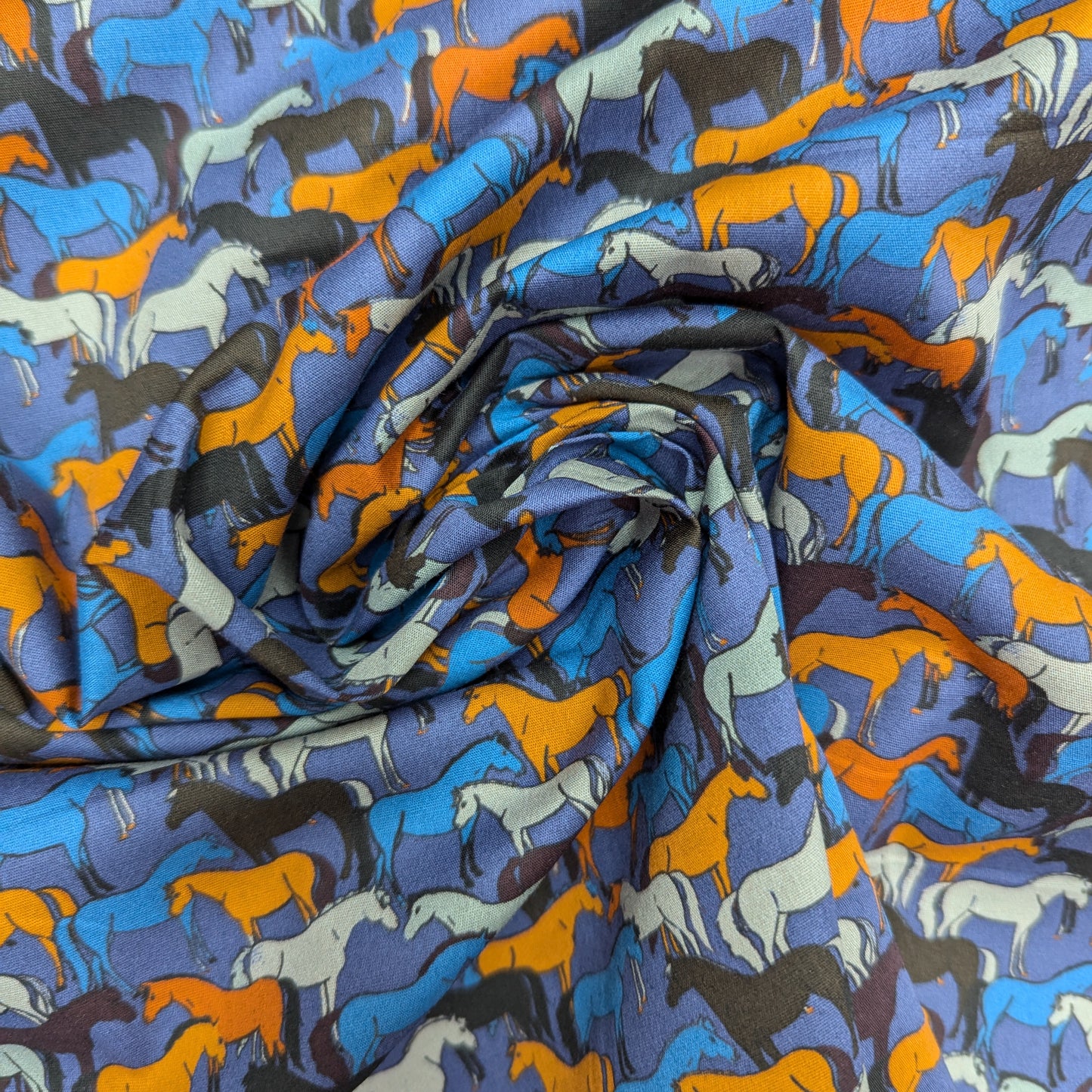 Deadstock cotton poplin fabric with colorful horse silhouettes on a blue background.
