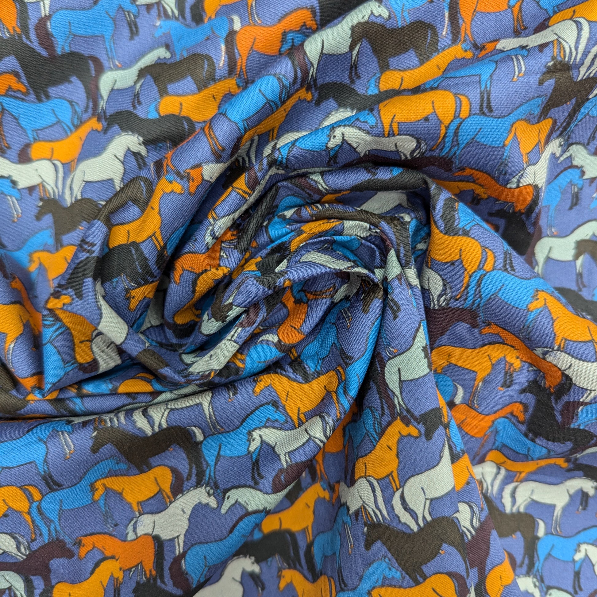 Deadstock cotton poplin fabric with colorful horse silhouettes on a blue background.