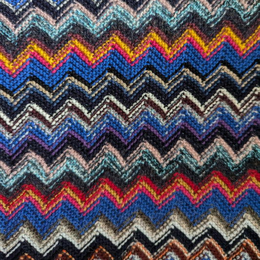 Colorful zigzag knit fabric in blue tones, red, yellow, and pink, showing soft texture.
