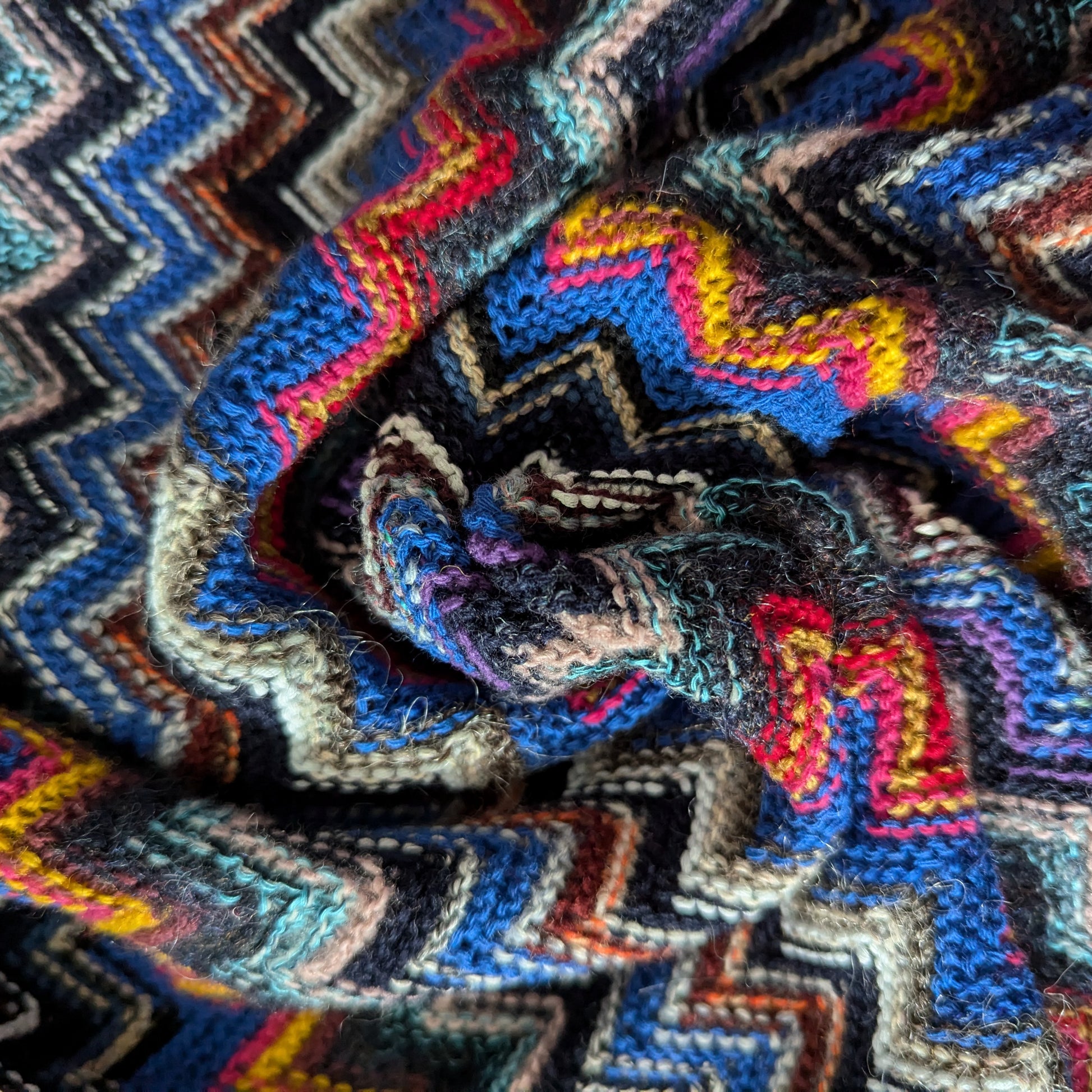 Colorful deadstock knit fabric with a vibrant zigzag pattern in blue tones, red, and yellow.