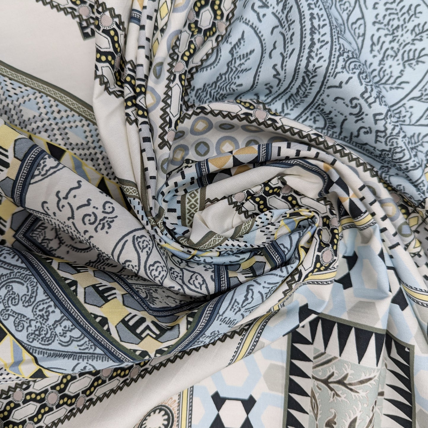 Deadstock cotton poplin fabric with a multi-color geometric and paisley pattern in blues, grays, and yellows.