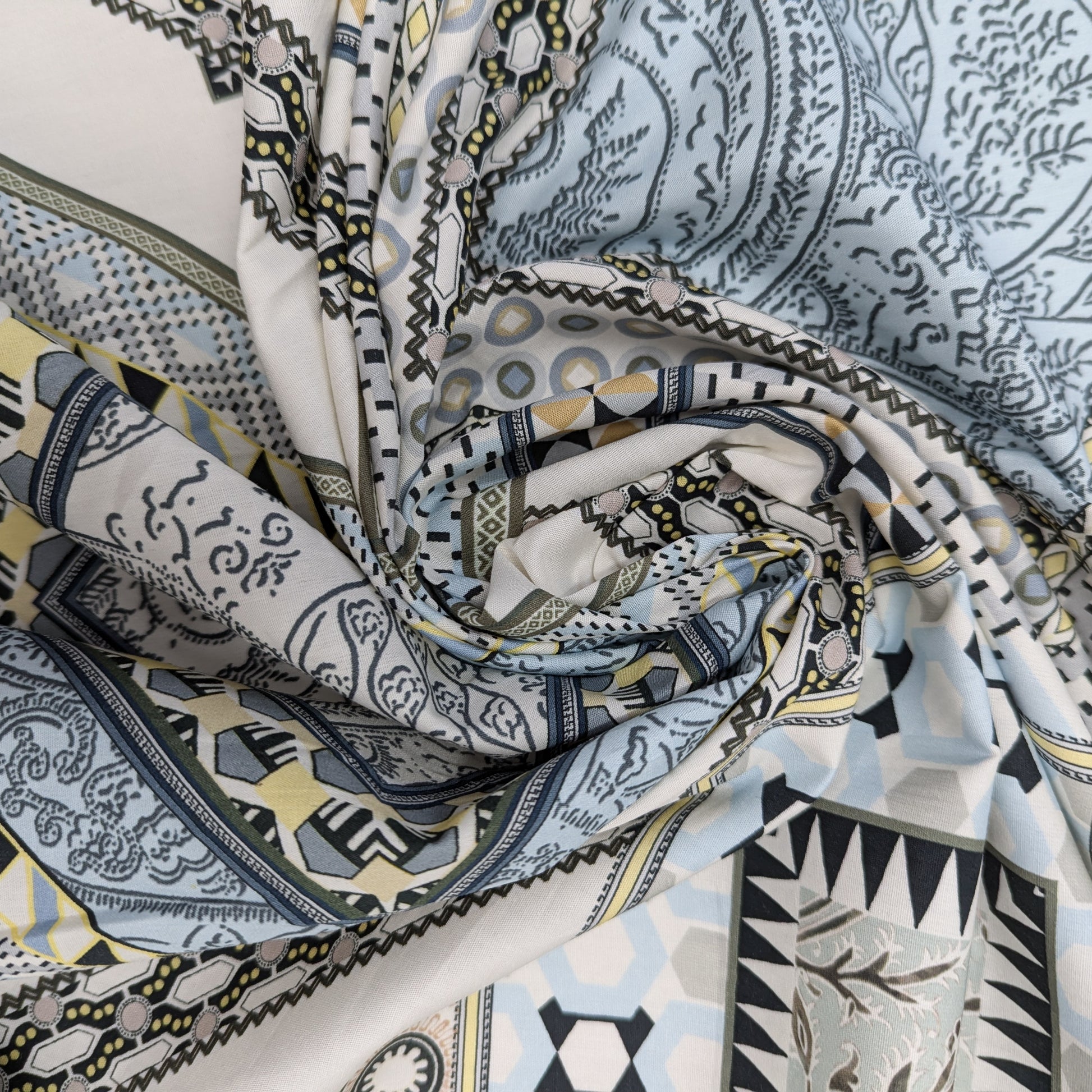 Deadstock cotton poplin fabric with a multi-color geometric and paisley pattern in blues, grays, and yellows.