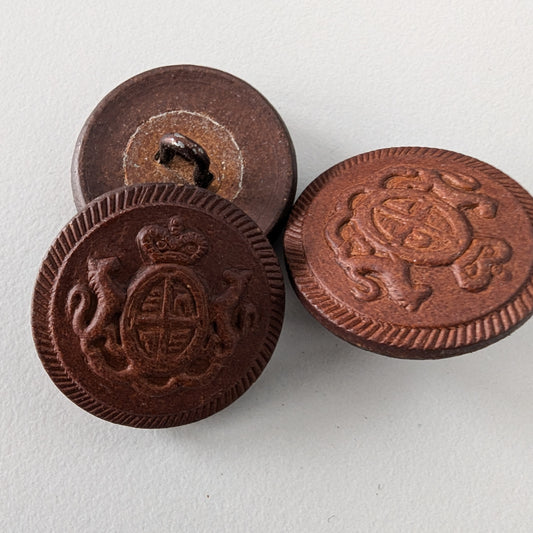 Three 2.5 cm dark brown Bongossi wood buttons with intricate embossed crest designs.