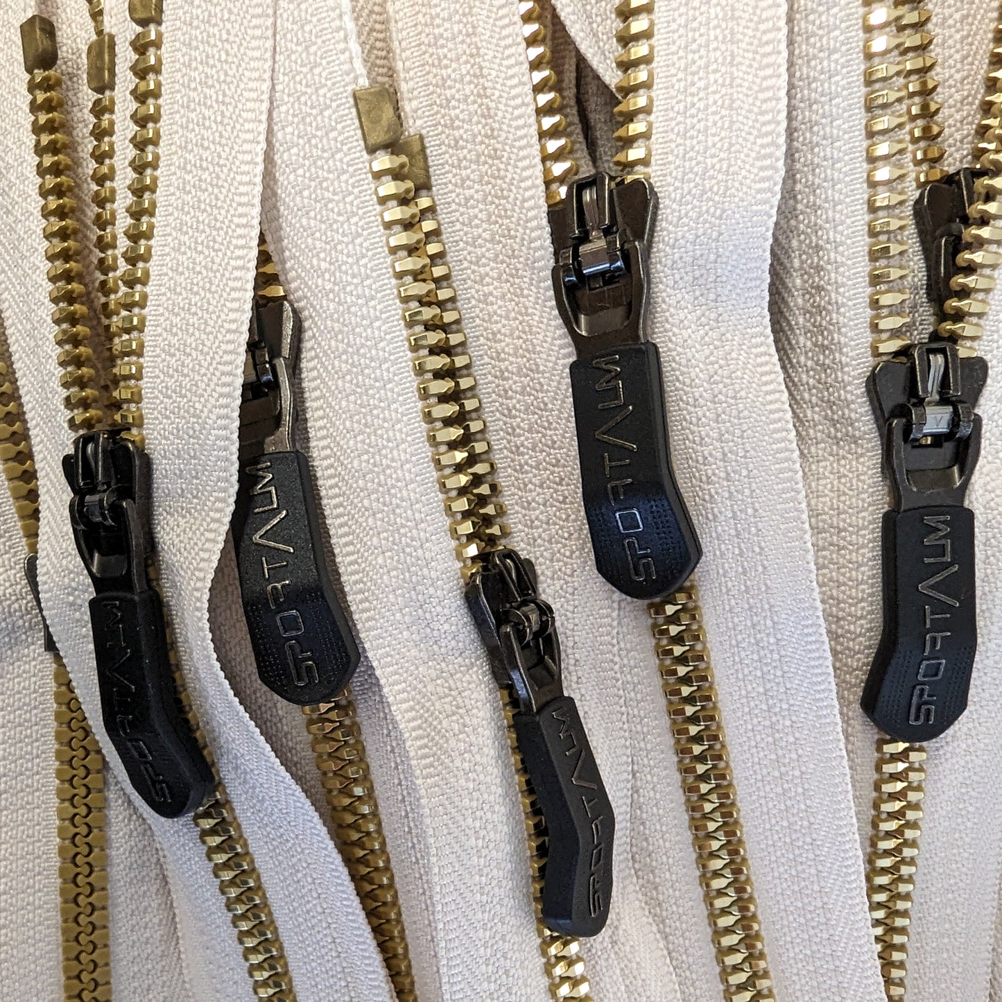 Cream zipper with golden metal teeth and black "SPORTALM" designer pullers.