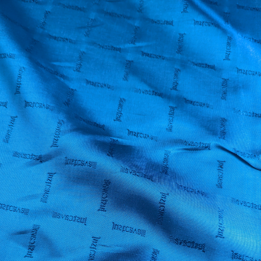 Smooth Chionose blue deadstock viscose lining fabric by Jst Cavall, featuring a subtle repeating brand name and a light sheen.