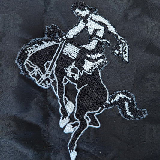 Black and white embroidered cowboy riding a bucking horse patch, 15x20cm, on a black fabric background.