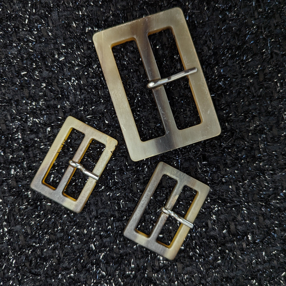 Set of three matte horn-look resin trench coat buckles: one large, two small, on black fabric.