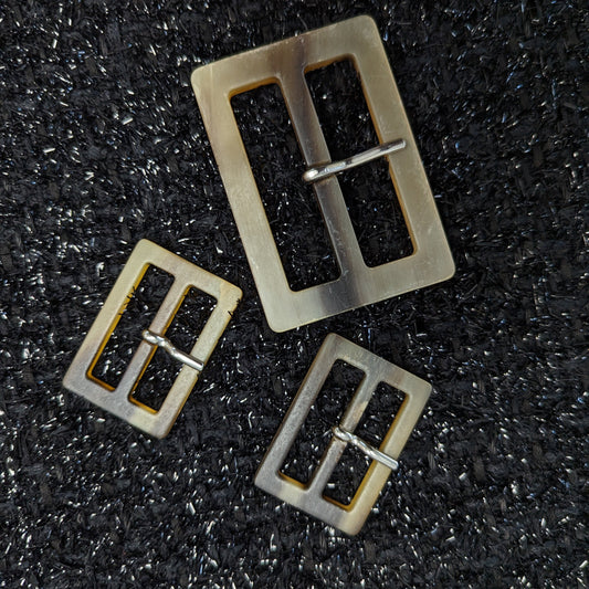 Set of three matte horn-look resin trench coat buckles: one large, two small, on black fabric.