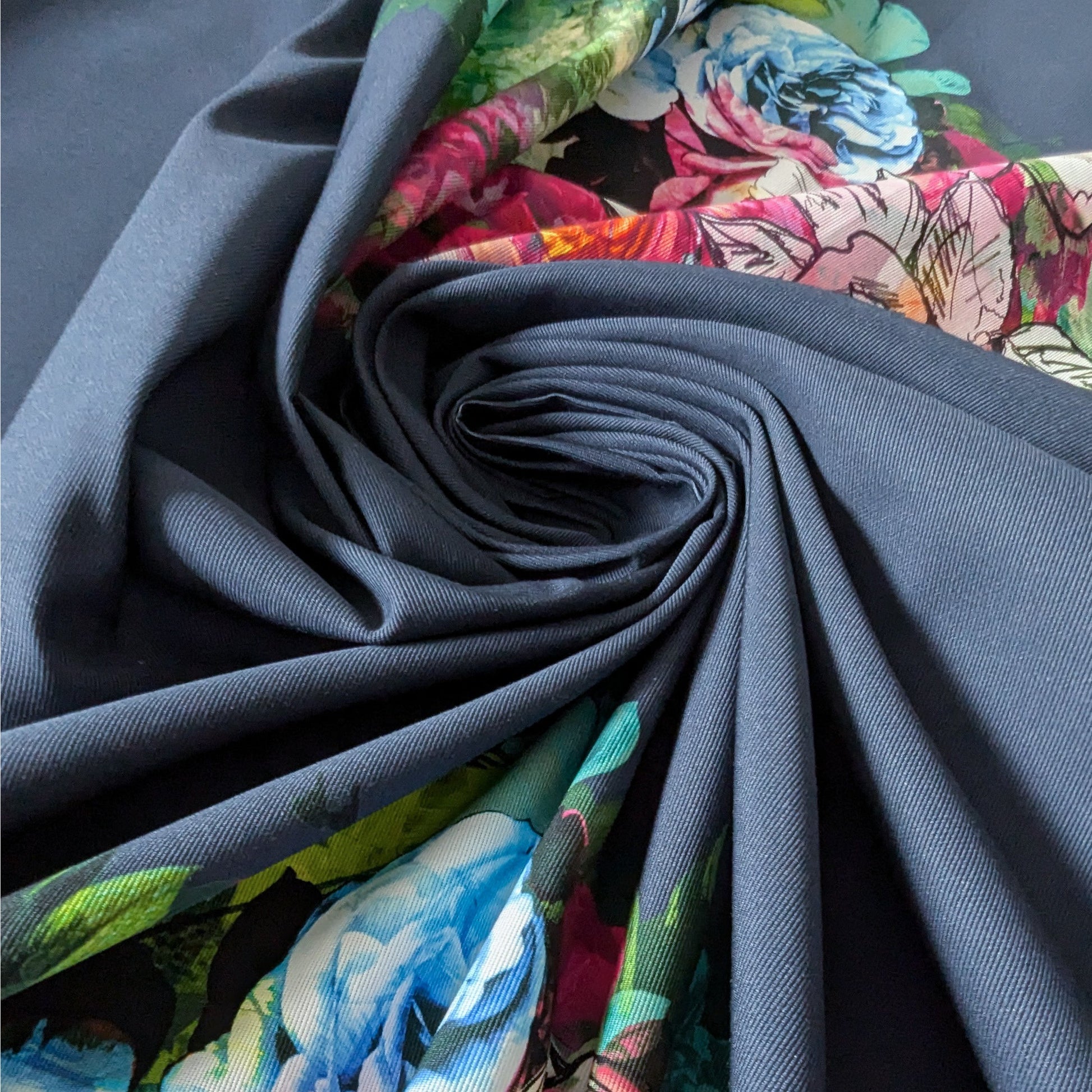 Deadstock denim fabric, navy blue with vibrant floral panels, spiraled.
