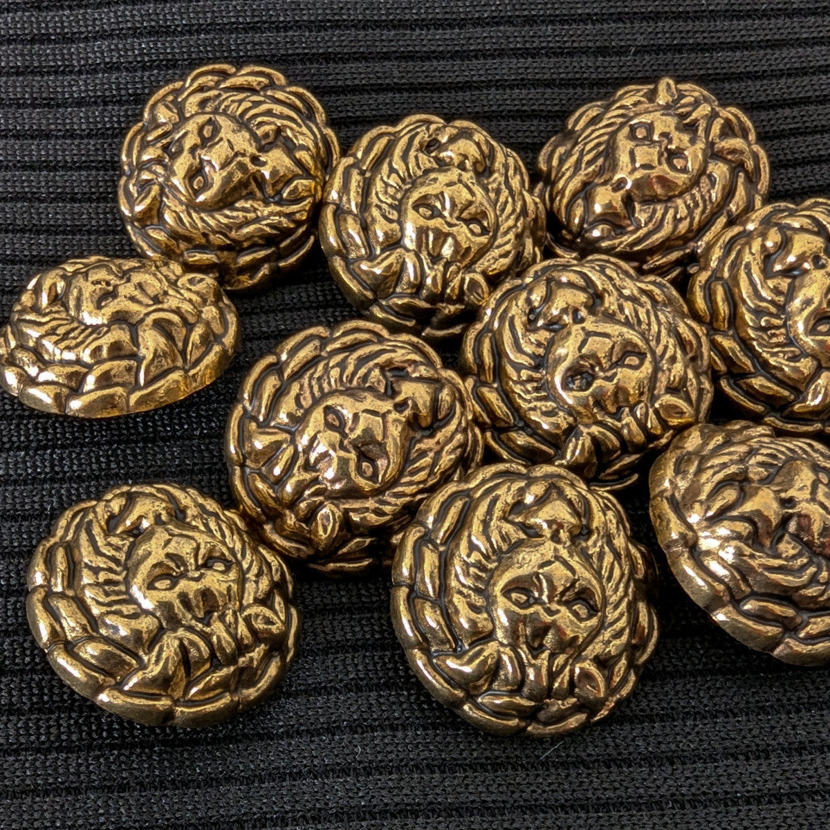 Ten vintage brass Gianni Versace lion head buttons, 1.7cm, on a black ribbed fabric.