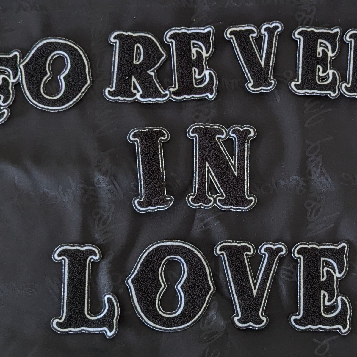 Black chenille "FOREVER IN LOVE" patch set with white embroidered outlines, on a dark fabric.
