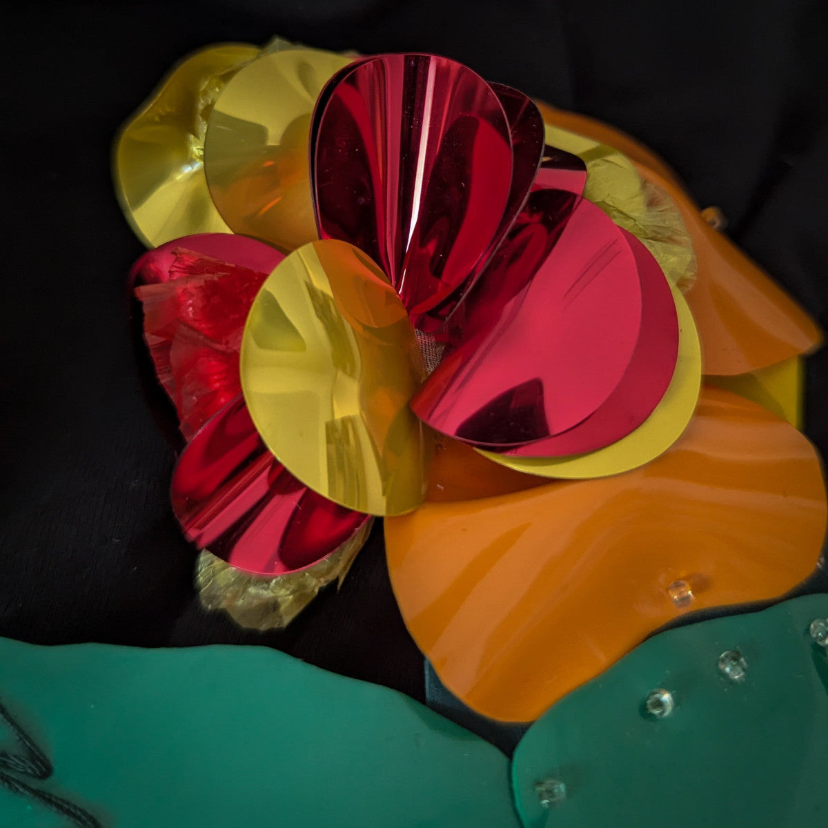 Shiny red, yellow, and orange plastic flower patch with green leaves and clear embellishments.