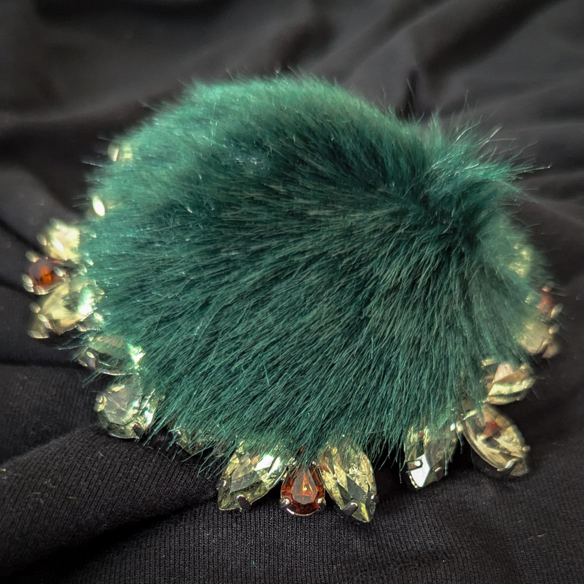 Dark green fur ornament with clear and amber Swarovski crystals on black fabric.