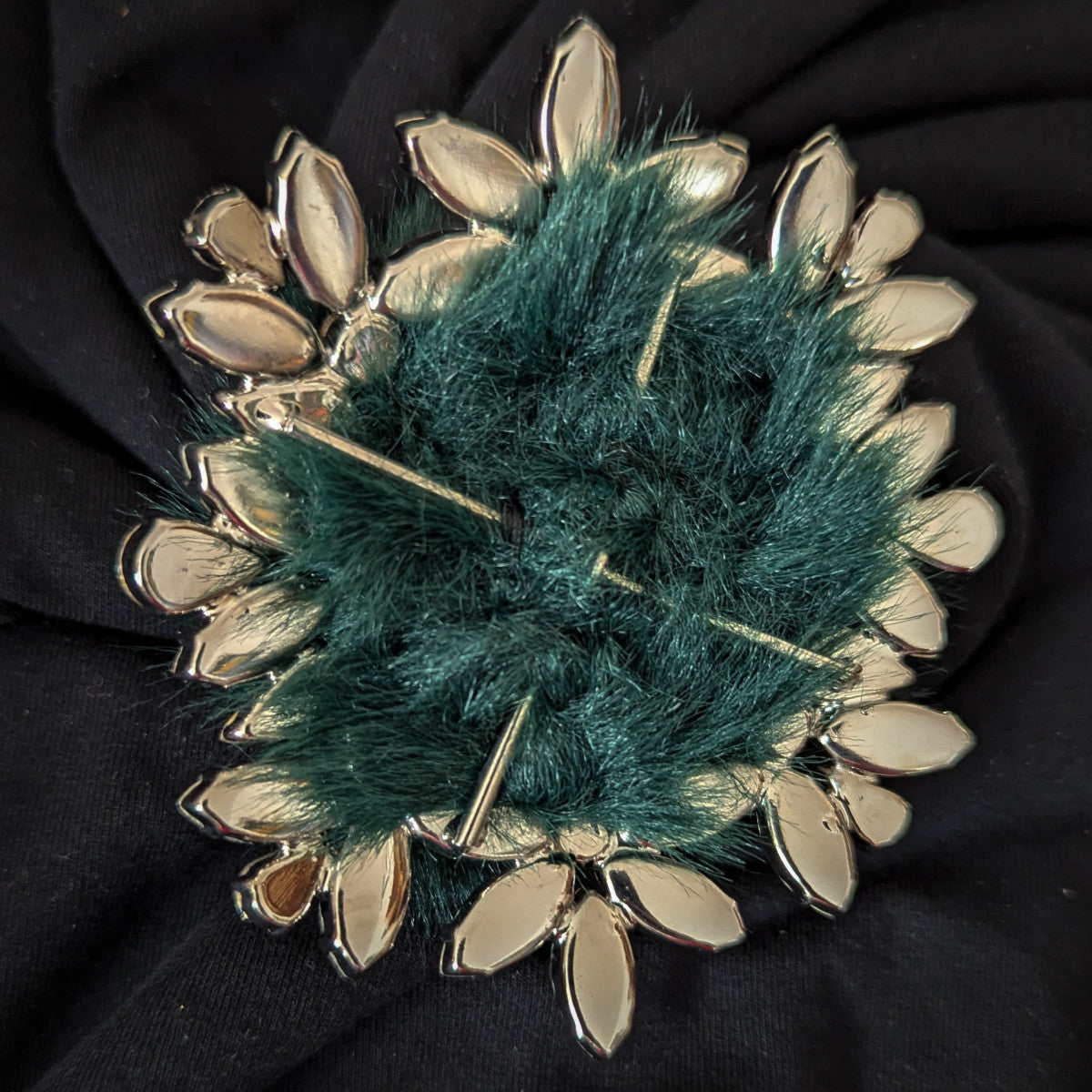 Gold-tone Swarovski crystal ornament with dark green faux fur, 9cm x 9cm, on black fabric.