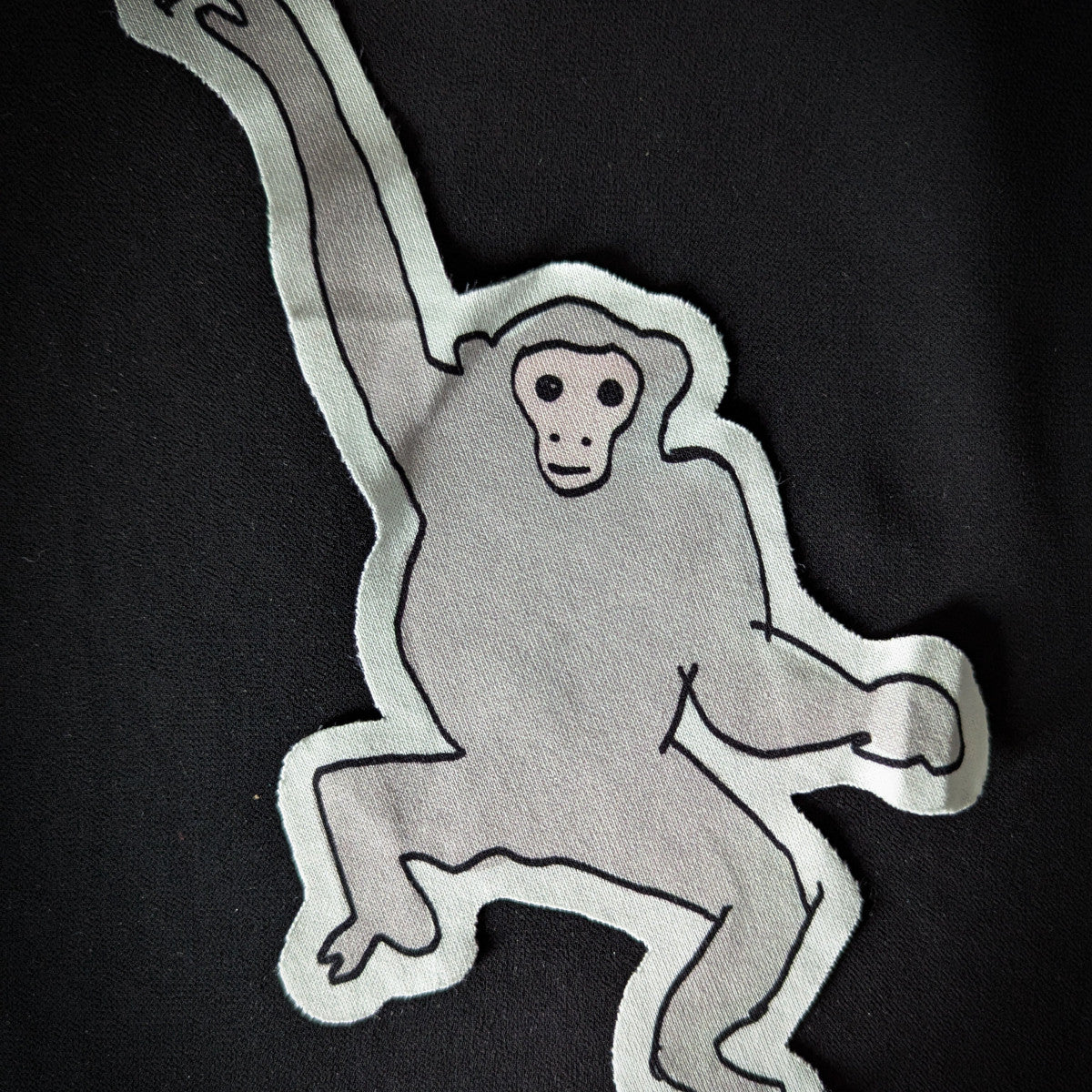 Gray monkey patch with black outline, 14x22cm, on a black background.