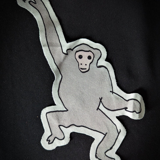 Gray monkey patch with black outline, 14x22cm, on a black background.