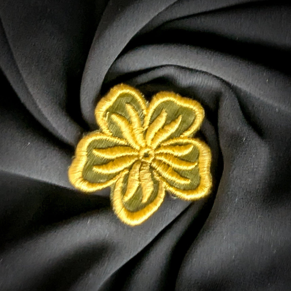 Embroidered floral patch, 5x5 cm, with yellow and olive green threads on dark fabric.