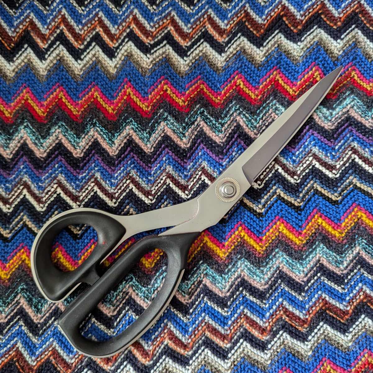 Colorful zigzag knit fabric in blue tones with black-handled scissors.