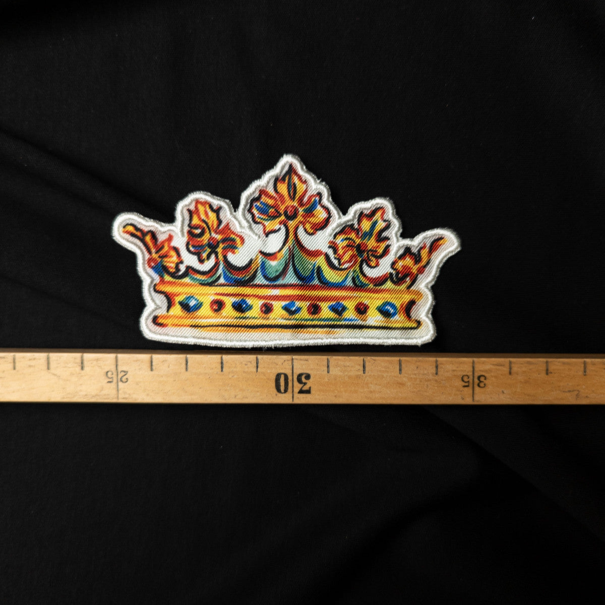 Colorful embroidered D&G crown patch, 10cm wide, on black fabric with a ruler.
