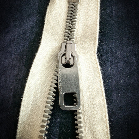10 cm D&G metal zipper with cream tape, engraved logo slider, and silver teeth.
