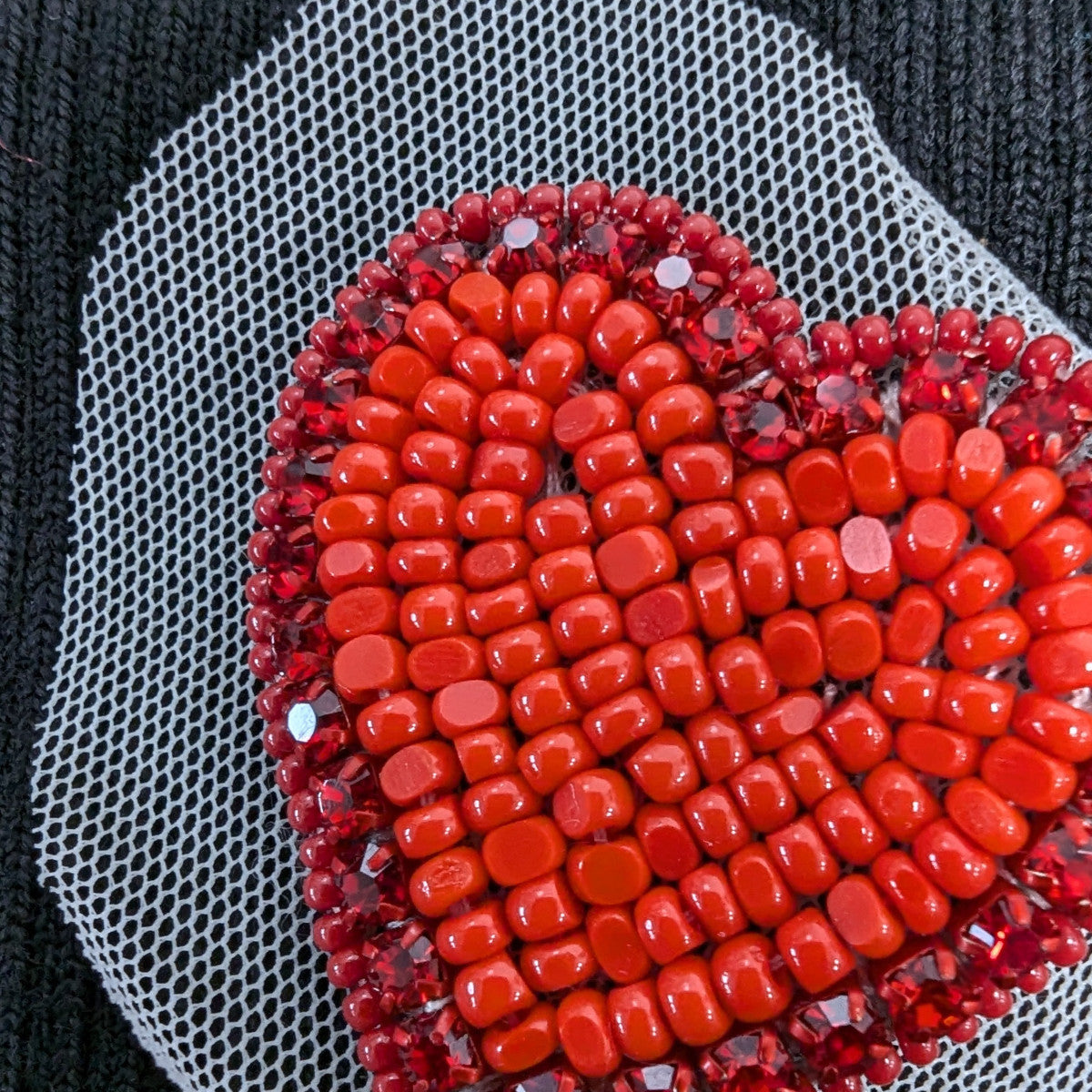 Red crystal heart patch with hand-sewn stones on white mesh, ideal for clothing or accessories.