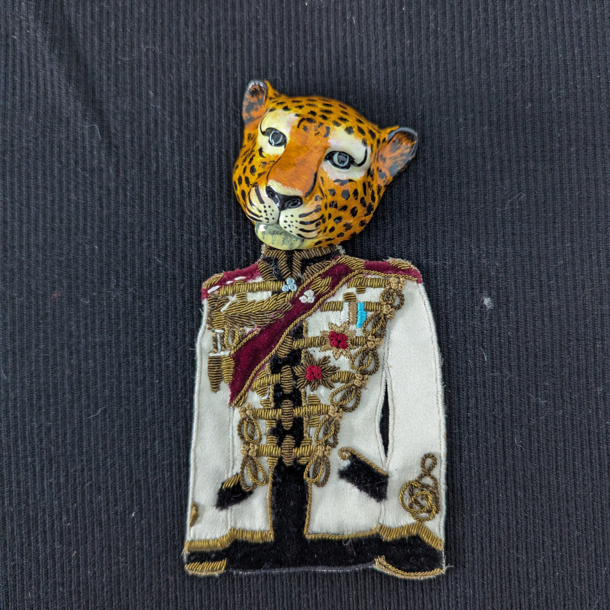 D&G leopard head patch in a white military uniform with gold embroidery, red sash, and medals.