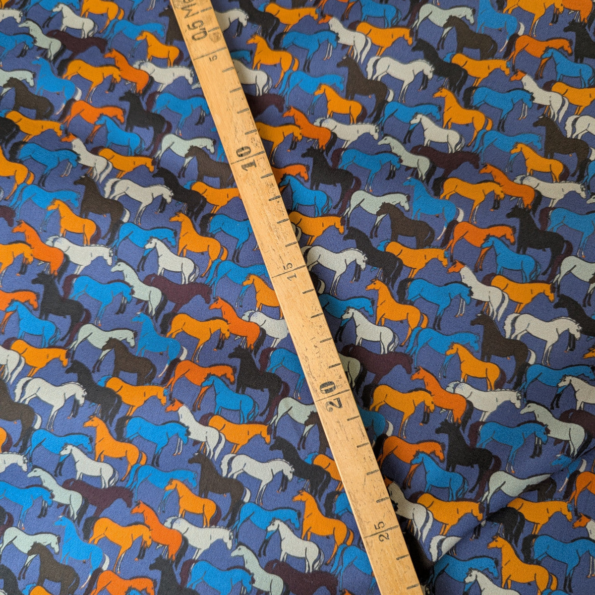 Blue cotton poplin fabric with colorful horse silhouettes and a wooden ruler.