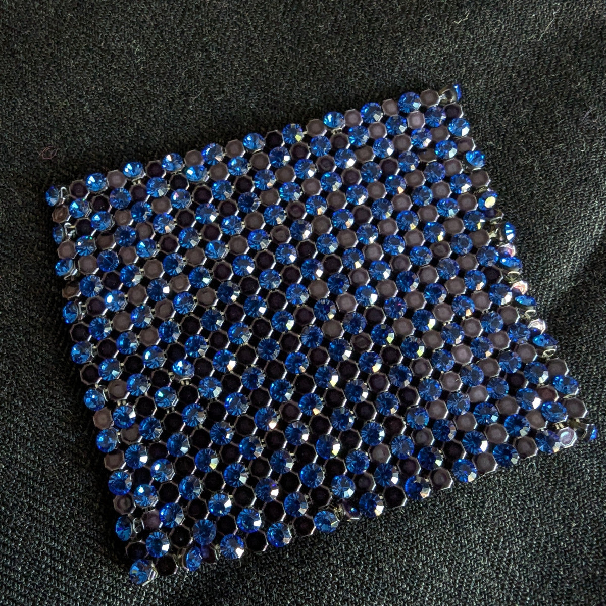 D&G Swarovski & Kristall patch with alternating blue and dark gray rhinestones on a dark fabric.