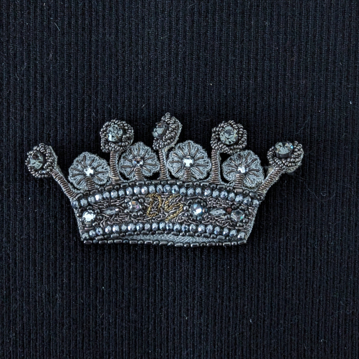 D&G embroidered crown patch with silver beads, pearls, and jewels on black fabric.