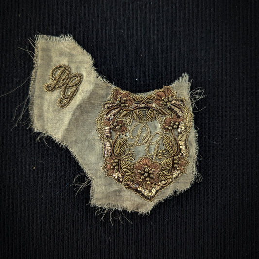 D&G gold metal embroidery patch, 7x6cm, with floral shield logo on light fabric.