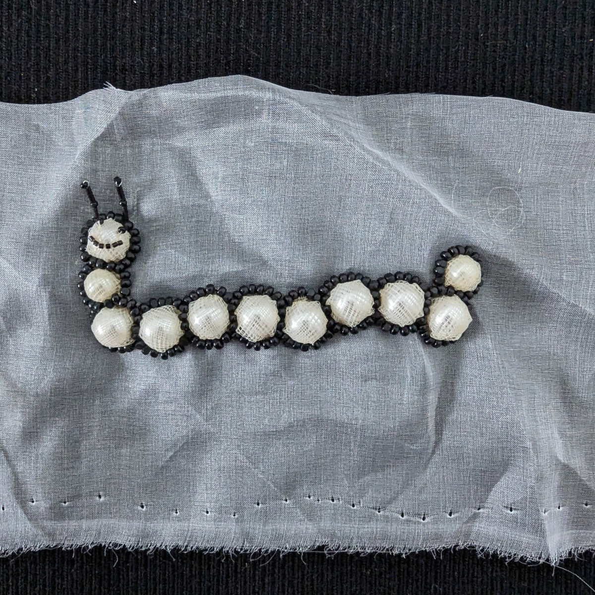 D&G 10cm pearl and black bead caterpillar patch on white fabric.