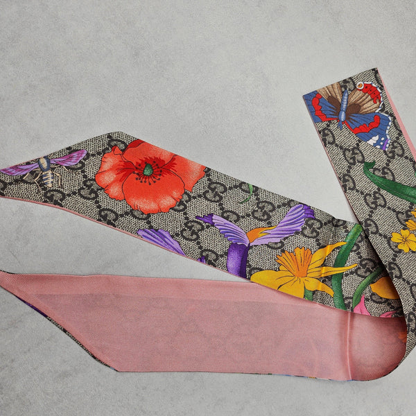 Gucci silk twilly with GG logo, vibrant floral, butterfly, and bird print, and a pink reverse side.