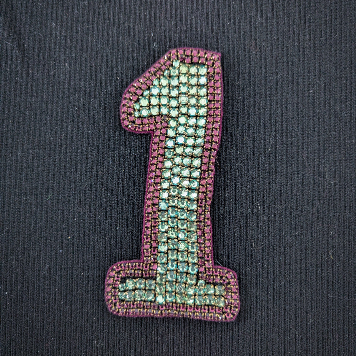 D&G "1" patch with sparkling turquoise beads and a purple embroidered border on black fabric.