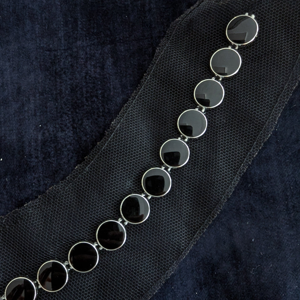 Silver chain with round black enamel or pearl patches, resting on dark fabric.