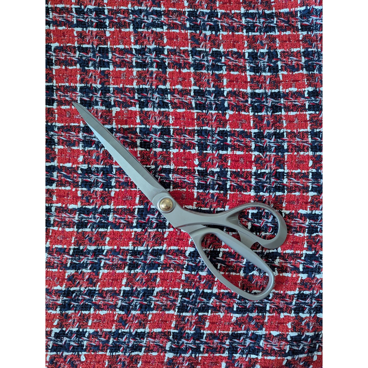 Red, black, and white plaid tweed fabric with a pair of grey sewing scissors.